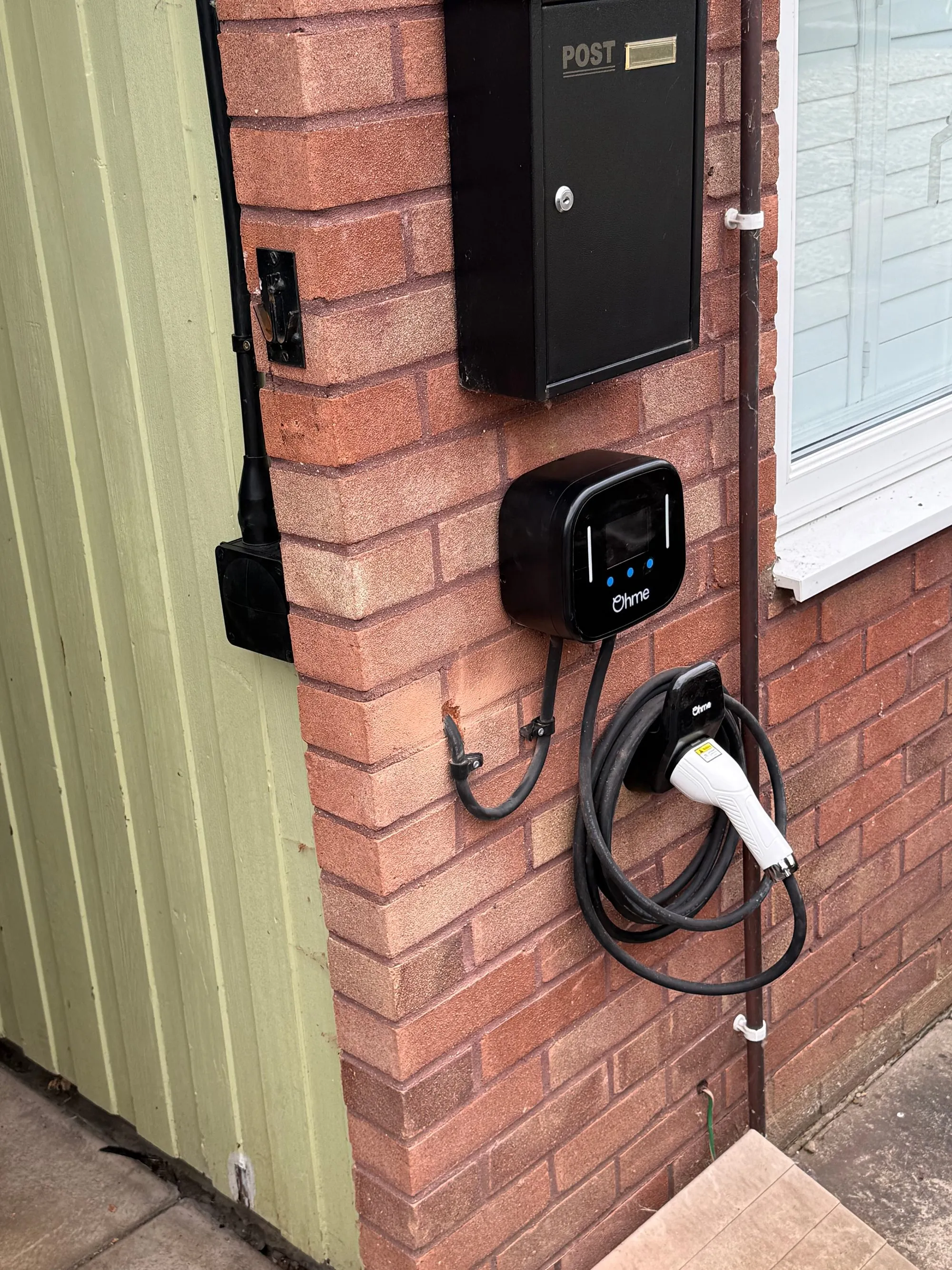 Ohme Home Pro EV charger installed on a brick wall by the front door in Fownhope