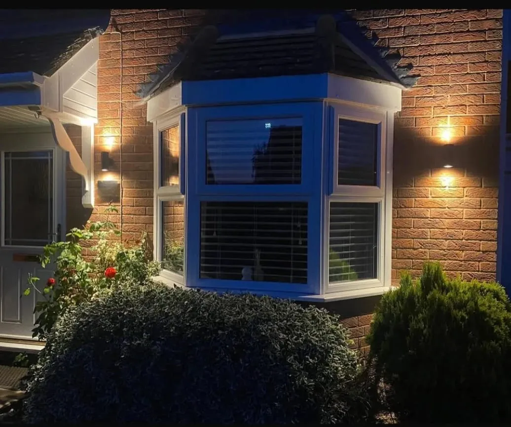 Up and down wall lights lighting the bay window and porch of a Credenhill house at dusk